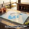 A glass cutting board featuring a Reelfoot Lake, Tennessee map and compass design rests on a wooden dock.
