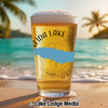 Glass of beer with "Oneida Lake" text and compass design on a beach.