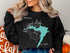 Black sweatshirt with a teal map of Rushford Lake, New York and compass.