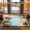 A glass cutting board displaying a map and compass design for Parker Canyon Lake, Arizona, surrounded by crackers, cheese, and pecans on a wooden table.