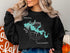 Black sweatshirt with a teal map of Lake Cachuma and compass rose.