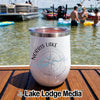 A white stainless steel insulated tumbler with Norris Lake Tennessee compass design sits on a wooden boat deck with people in the water.