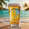 Glass of beer with "Lake Charleston" and compass graphic on beach at sunset.