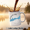 White mug with Geneva Lake and compass design, pouring coffee, Lake Lodge Media logo.
