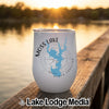 A white stemless wine tumbler with a compass design and the text Moss Lake North Carolina sits on a wooden dock with a lake sunset background.