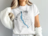 Cayuga Lake map graphic with compass rose and New York text on white t-shirt.
