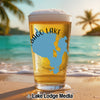 Glass of beer with map design on beach with palm trees and ocean.