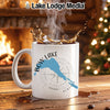 White mug with "Bow Lake Alberta" design and compass rose, next to a fireplace.