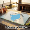 A rectangular glass cutting board featuring a blue map of Lake Okeechobee, Florida, sits on a wooden dock with drinks and lime slices nearby.