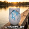 A white travel tumbler with a blue map of Lake Massabesic, New Hampshire, sitting on a wooden dock at sunset.