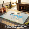 A rectangular glass cutting board featuring a blue map of Lake Spivey, Georgia, rests on a wooden dock with copper mugs and limes nearby.