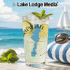 Tall glass with drink, limes, and mint on a beach with a sailboat.