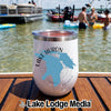 A white tumbler featuring a blue map of Lake Huron sits on a boat deck with people swimming in the background.