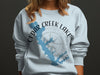 Light blue sweatshirt with "Cedar Creek Lake Texas" text and lake outline graphic.