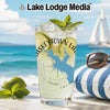 Glass with drink, limes, mint, and compass design on beach with sailboat.