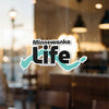 "Minnewanka Life" logo with a teal outline in the shape of a lake, on glass.