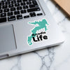 Teal map sticker with black "Arcadia Life" text on laptop keyboard
