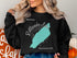 Black sweatshirt with a teal outline of Rattlesnake Lake and compass rose.