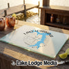 A tempered glass cutting board featuring a blue map of Lake Lotawana, Missouri, and a compass rose rests on an outdoor wooden bar.