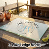 A rectangular glass cutting board with a compass and The Finger Lakes New York design sits on a wooden dock.