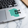 Teal sticker with black text "Red Life" on a laptop keyboard.