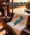 Trout Lake map blanket on brown leather sofa with fireplace and lake view.