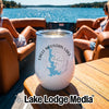 A white insulated wine tumbler with an Eagle Mountain Lake map graphic rests on a wooden table aboard a boat with two women seated in the background.