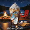 Glass of coffee with whipped cream, campfire, lake, chair, and s'mores ingredients.