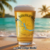 Beer glass with Sakakawe map and compass on a beach with palm trees and ocean.
