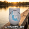 A white stemless wine tumbler rests on a wooden dock with a lake sunset background.