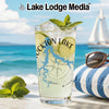Glass with cocktail, lime slices, mint, and lake map design on beach background.