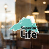 Teal map outline sticker with "Superior Life" text, on a window.