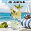 Glass with drink, limes, and mint on a beach with a sailboat in the background.
