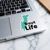 Teal map outline sticker with black "Trout Life" text on a laptop