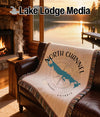 White blanket with North Channel and compass design on brown leather couch.