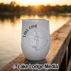 A white travel tumbler featuring a Lake Oahe compass design sits on a wooden dock at sunset.