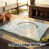 A glass cutting board with a Chickamauga Lake compass design rests on a wooden dock with drinks.