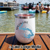 A white insulated tumbler featuring a Spoon Lake Illinois compass design sits on a wooden surface near water.
