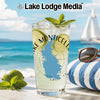 A tall glass of lemonade with mint and lime sits on a table outdoors near a beach, sailboat, and sunglasses.