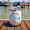 A white stainless steel tumbler with Flagstaff Lake Maine design rests on a wooden dock with lake and boats in the background.