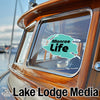 Turquoise "Monroe Life" sticker on a wooden boat window with "Lake Lodge Media" text below.
