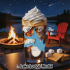 Glass of iced coffee with whipped cream, lake map design, and s'mores ingredients by a campfire.