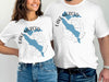 Two people wear white t-shirts with a blue Lake Merced shape on a compass graphic.