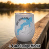 White stainless steel stemless wine tumbler with a blue map of Arcadia Lake, Oklahoma, resting on a wooden dock at sunset.