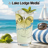 Glass with "Fort Peck Lake" design on beach with sailboat and sunglasses.