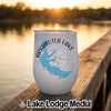 A white insulated wine tumbler with an Arkabutla Lake map graphic rests on a wooden dock at sunset.