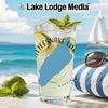 Glass with drink, mint, lime, and sunglasses on a beach with sailboat.
