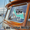 Turquoise Marion Life sticker on a wooden boat window, "Lake Lodge Media" logo below.