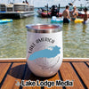 A white tumbler with a Lake America logo sits on a wooden dock with people boating in the background.
