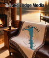 Blanket with Hudson Lake map and compass on a leather sofa, fireplace nearby.